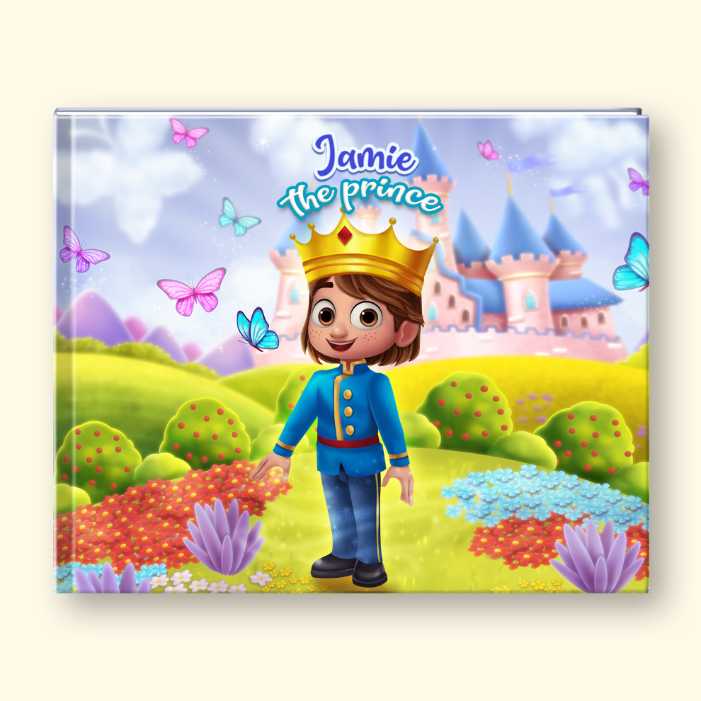 A personalized children's picture book cover featuring a cartoon prince in a blue uniform and gold crown standing in a colorful fantasy landscape with a castle, flowers, butterflies, and the text 'Jamie the prince'. The book is photographed upright against a light cream background.